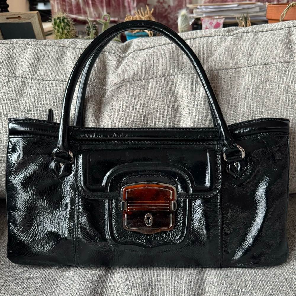 Elie Tahari black patent leather handbag with tortoise shell pocket opening.